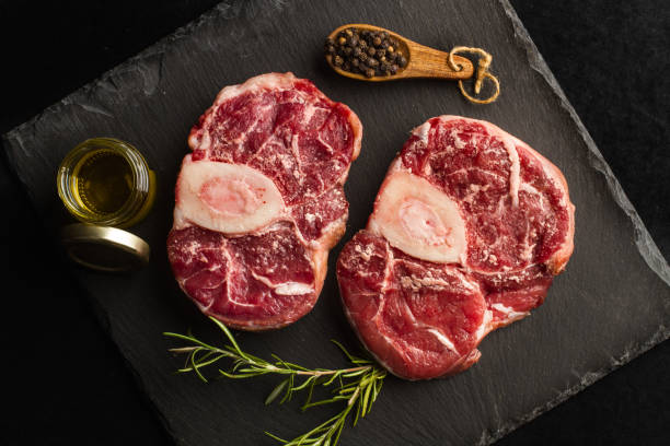 Raw osso buco slices in a black slab on a dark background